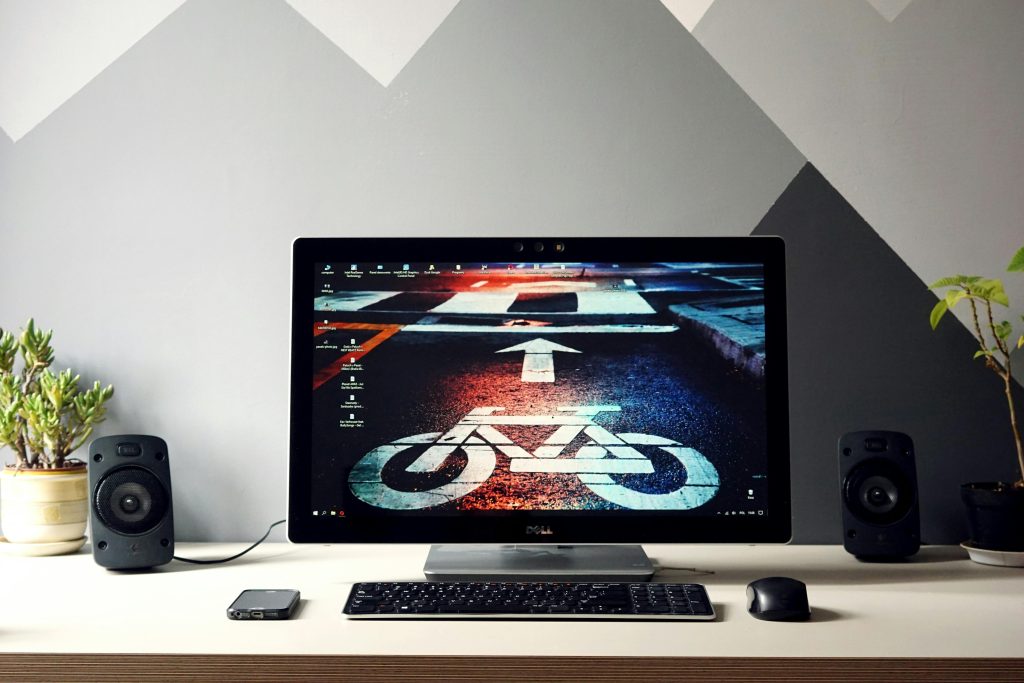 Sleek desktop setup featuring a monitor with urban cycling wallpaper, surrounded by speakers and plants.